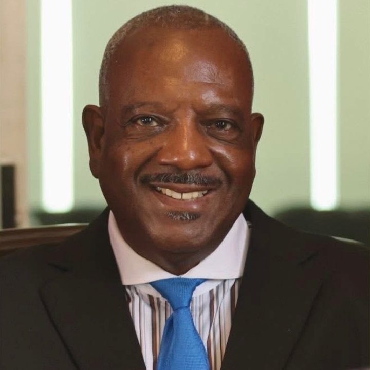 Deric A. Gilliard, Member at Large, smiling in a dark suit with a blue tie and a white pocket square.