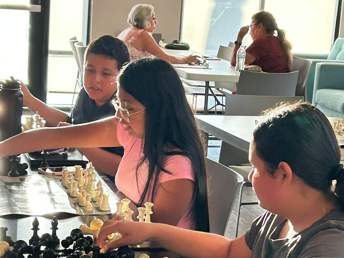 Children leaning over a chess board, one reaching out to move a piece, during a Chess at the Creek class.