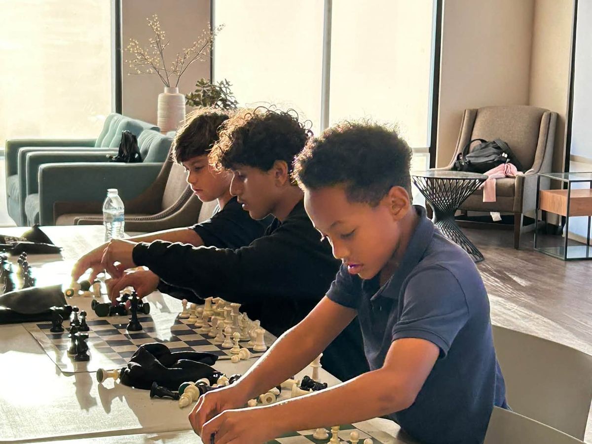 A young player reaching across the board to make a move while the other player watches.
