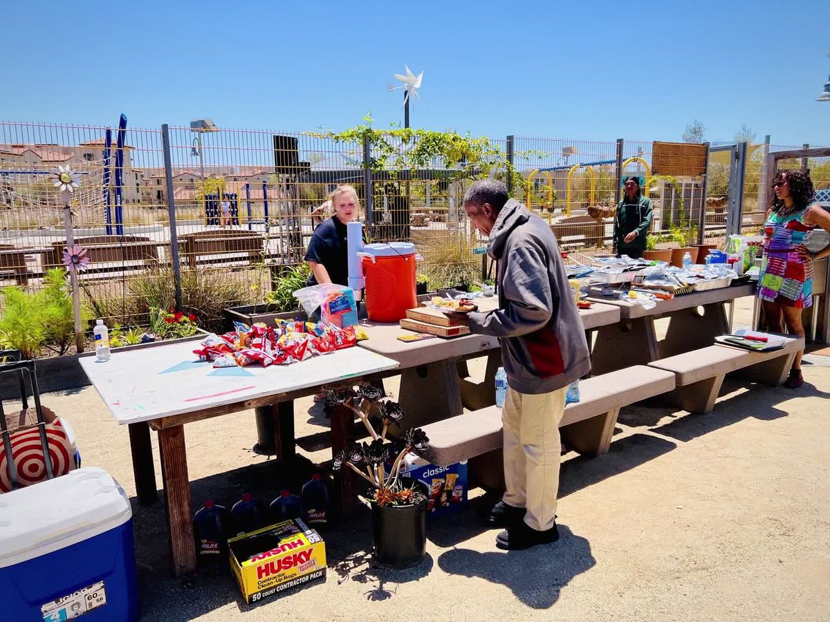 A line of neighbors waiting to be served a free meal at an outdoor community gathering.