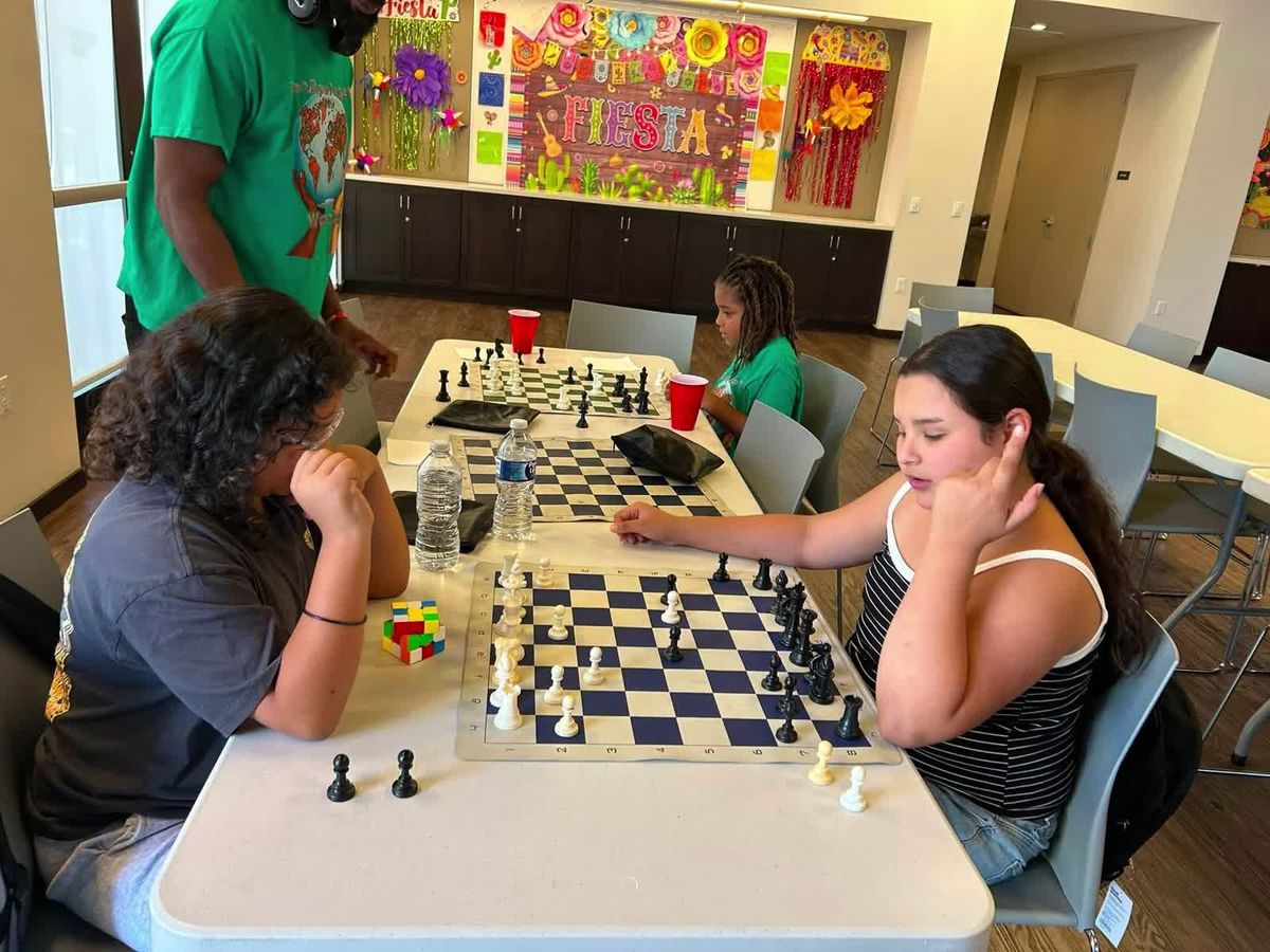 Children and adults seated across chess boards at long tables during a CCE family event.