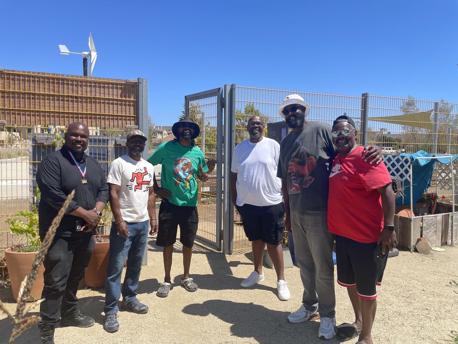 Community members standing together at the gate of a neighborhood garden beside raised planter boxes.