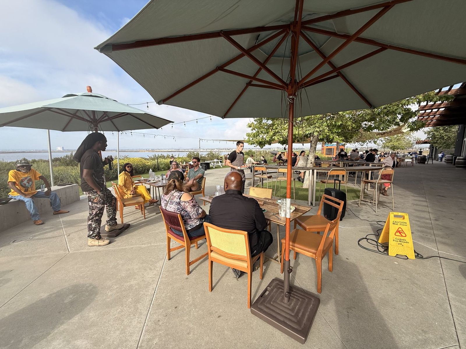 An outdoor community gathering on a patio with umbrellas, tables and neighbors in conversation.